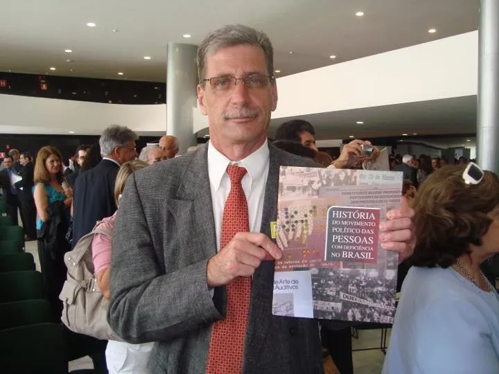 Antônio Campos de Abreu segurando o livro História do Movimento Político das Pessoas com Deficiência no Brasil durante evento.
