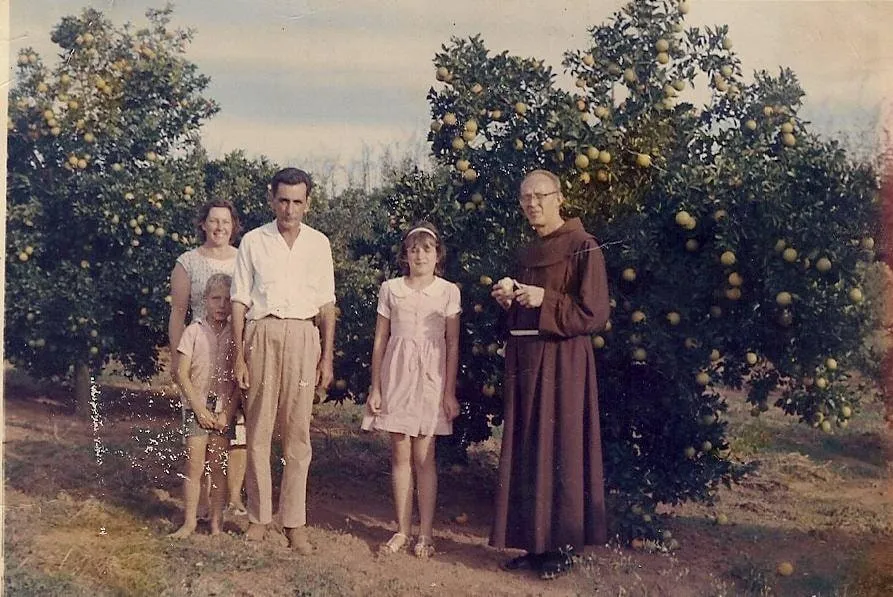 Família reunida em um pomar de laranjeiras ao lado de um frade, em ambiente rural.