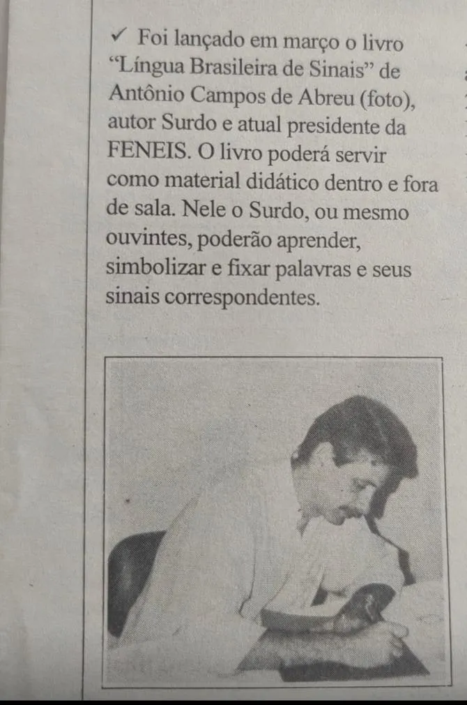 Recorte de imprensa noticiando o lançamento do livro Língua Brasileira de Sinais, de Antônio Campos de Abreu, com foto do autor autografando exemplares.